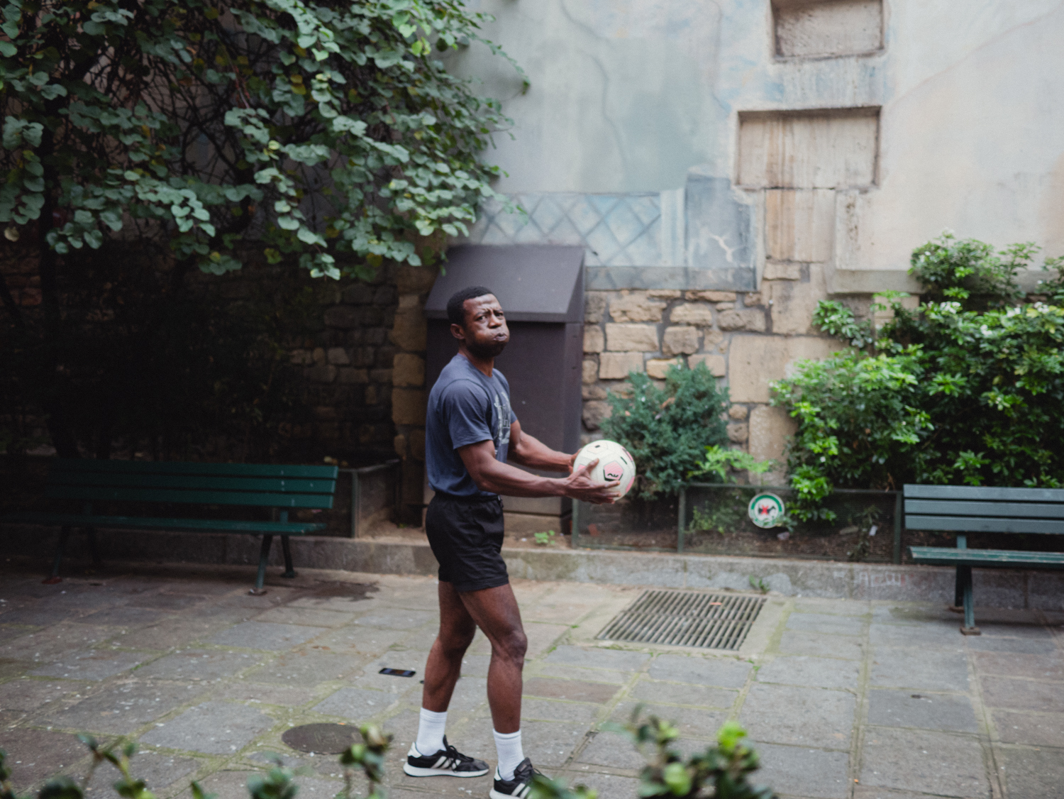 A man in purple t-shirt and black shorts catches a football with his hands while making an exhausting facial expression. 